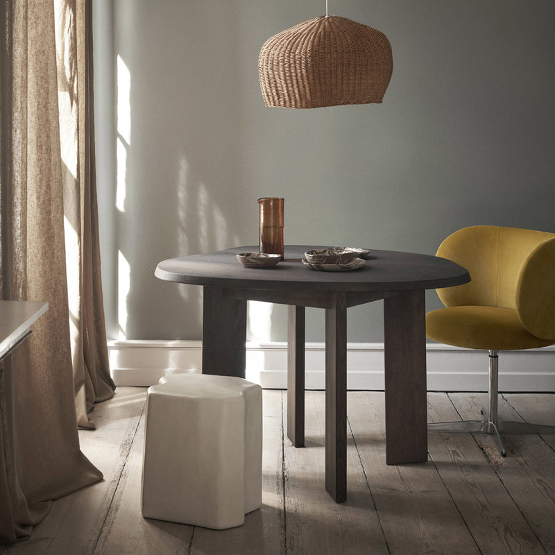 Round black table with a textured surface, yellow chair, and neutral-toned decor in a softly lit room.