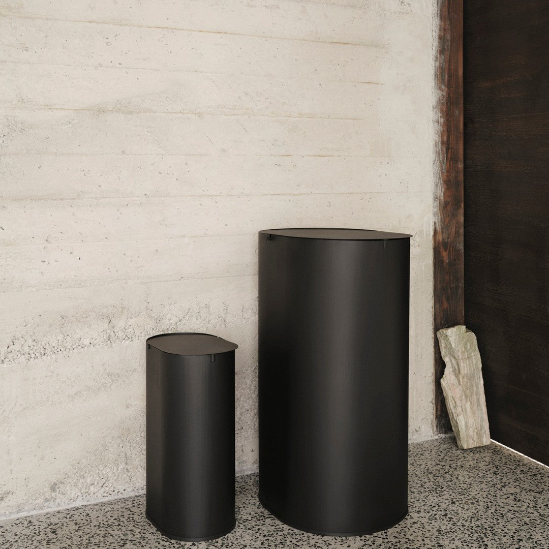 Two sleek black cylindrical containers against a textured concrete wall, showcasing a minimalist design.