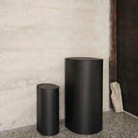 Two sleek black cylindrical containers against a textured concrete wall, showcasing a minimalist design.