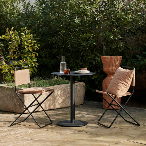 "Modern outdoor seating set with brown fabric chairs, black metal table, and terracotta vase amid lush greenery."