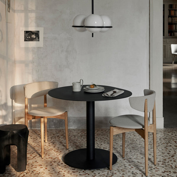 Elegant black round dining table with smooth surface, paired with light beige chairs featuring wood accents.