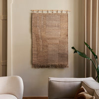 Textured beige wall hanging with subtle patterns and fringed edges, complementing neutral interior decor.