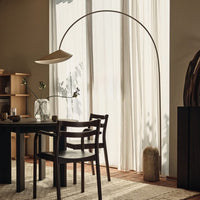 Modern arch floor lamp in beige, with minimalist black chairs and natural textures in a warm, neutral-toned interior.