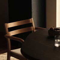 Light wood chair with a minimalist design next to a dark round table, featuring soft neutral tones in a modern setting.