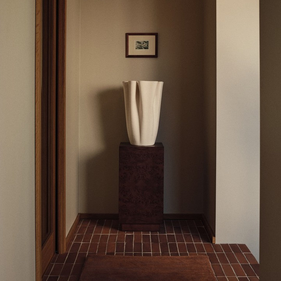 Elegant white vase on dark pedestal, contrasted against warm beige walls and earthy red brick flooring.