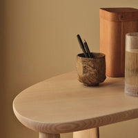 Soft beige tabletop with rounded edges, featuring a textured brown ceramic pot and a clear glass, against a neutral backdrop.