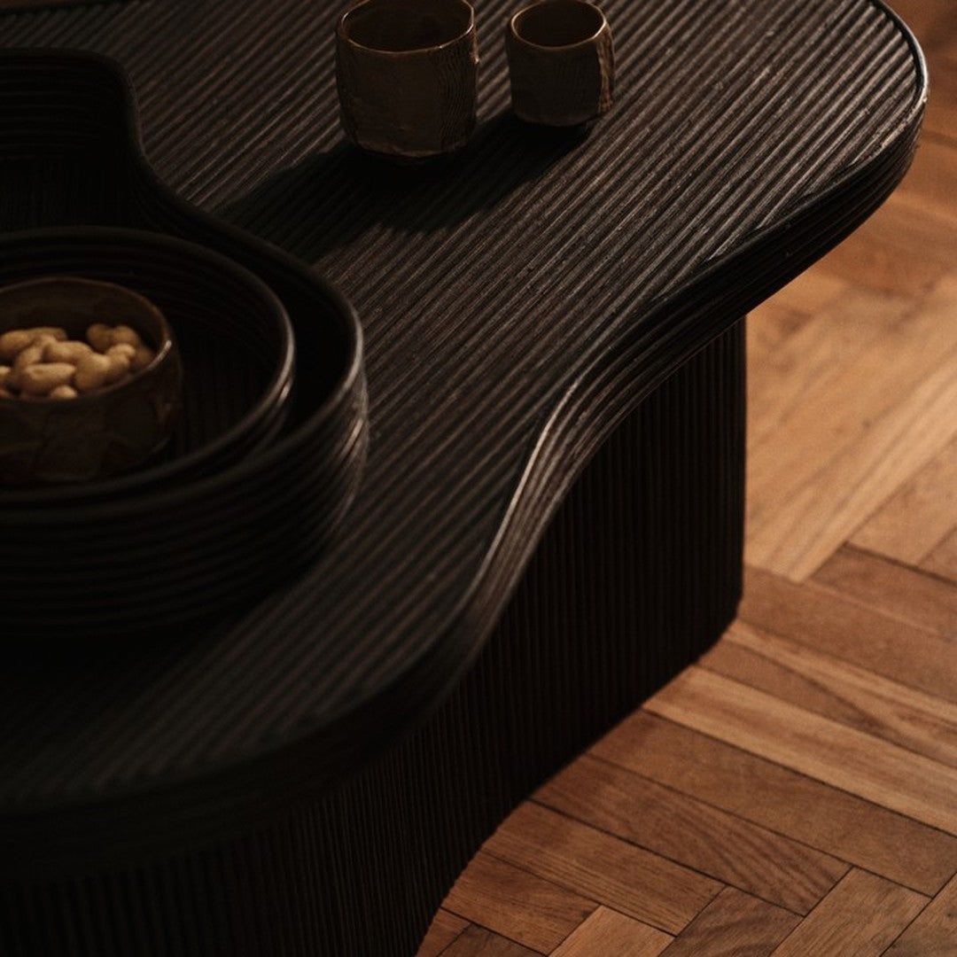 "Black ribbed texture table with circular bowls on a warm wooden floor, showcasing elegant patterns and contrasting colors."