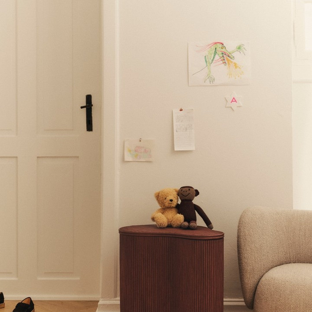 "Soft beige wall with simple wooden brown side table, featuring cuddly teddy bear decor."