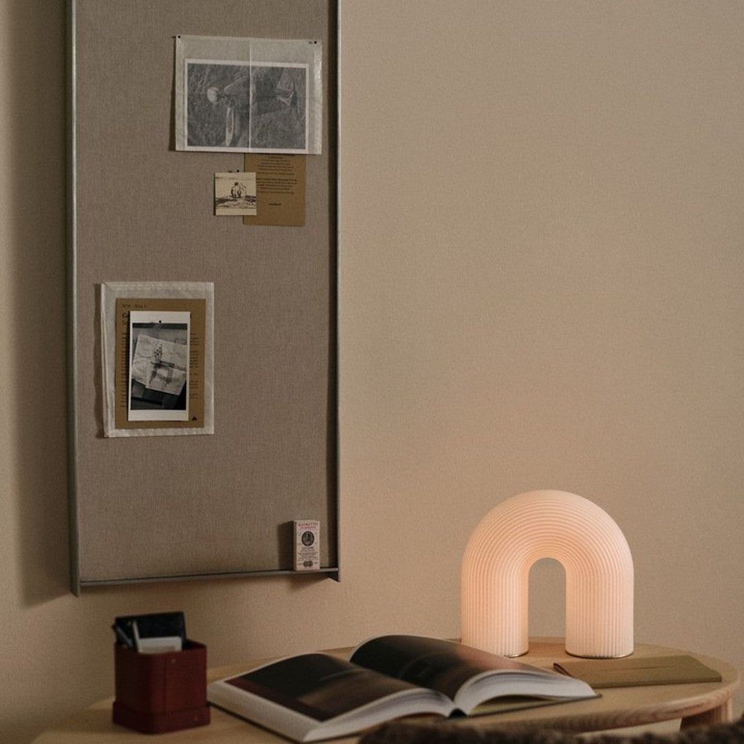Soft beige backdrop with a glowing white arch-shaped lamp, complemented by earthy tones in decor and dark photographic prints.