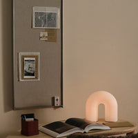 Soft beige backdrop with a glowing white arch-shaped lamp, complemented by earthy tones in decor and dark photographic prints.