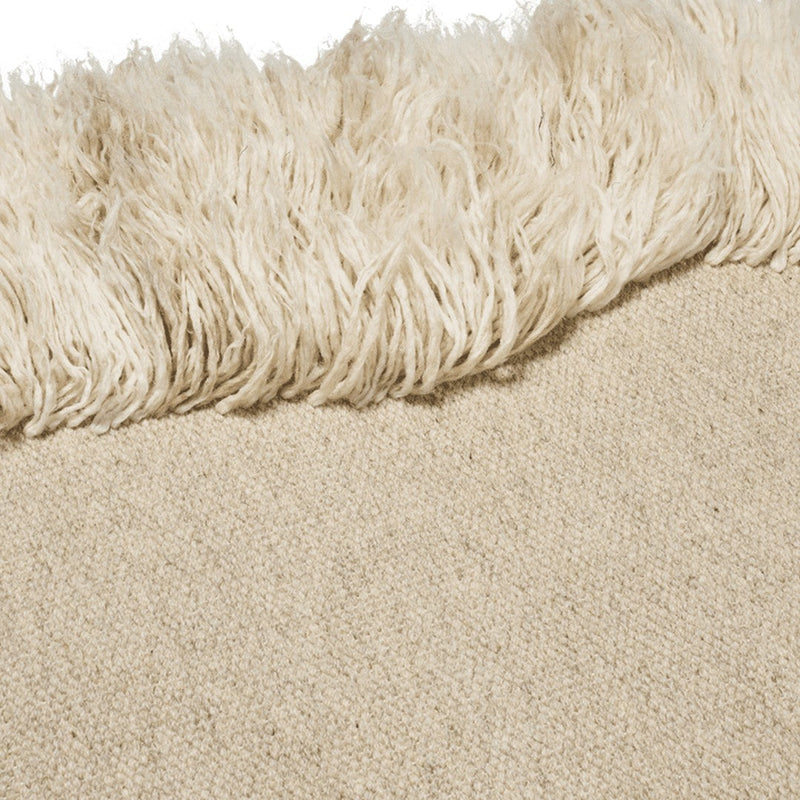 Beige woven rug with a textured, fluffy cream fringe detail. Subtle, neutral tones create a warm, inviting look.
