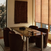 "Brown patterned wall hanging with warm wood tones, glass table, and rounded burgundy chairs in a cozy dining setting."
