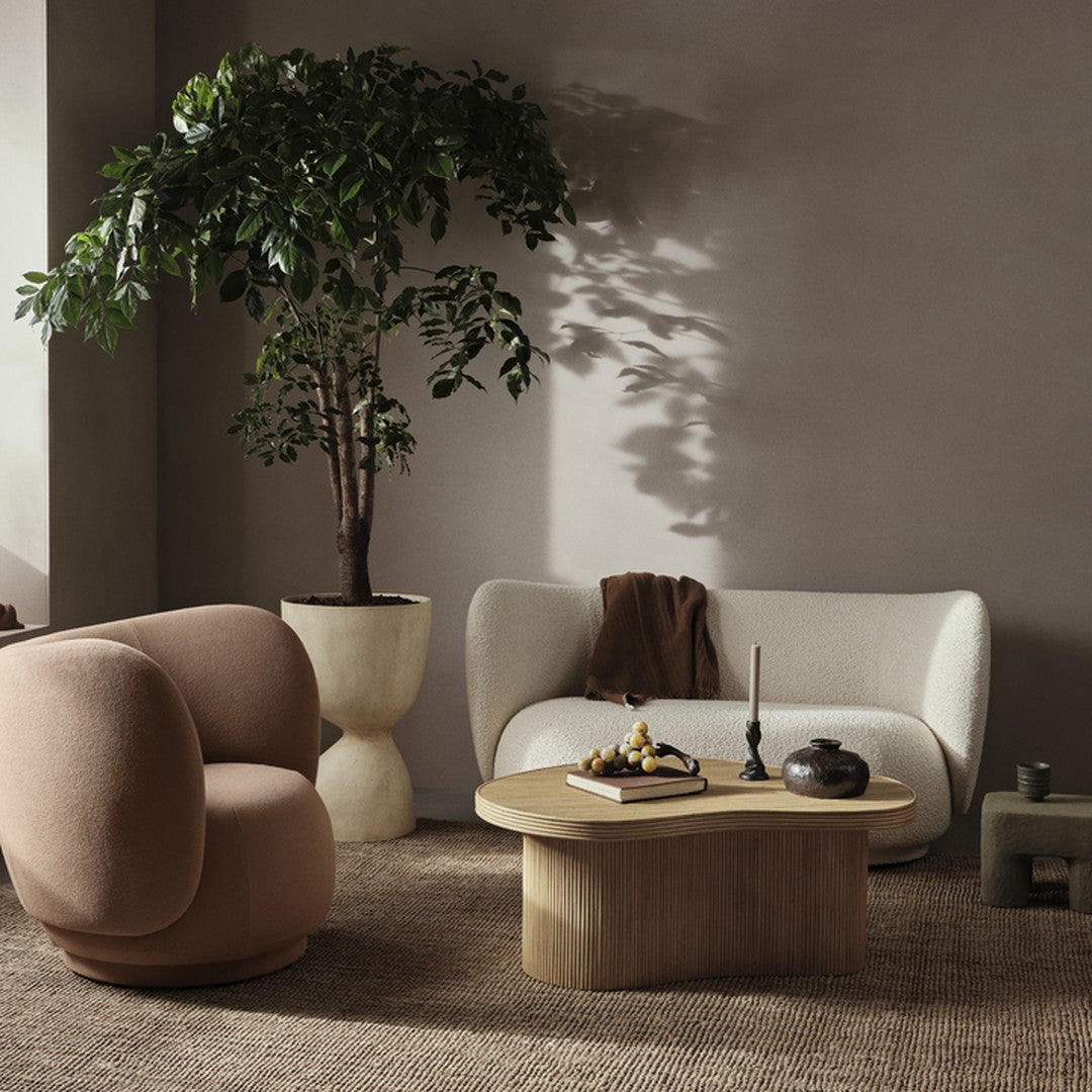 Curved beige armchair and soft white sofa with a natural wood coffee table against a neutral, textured backdrop.