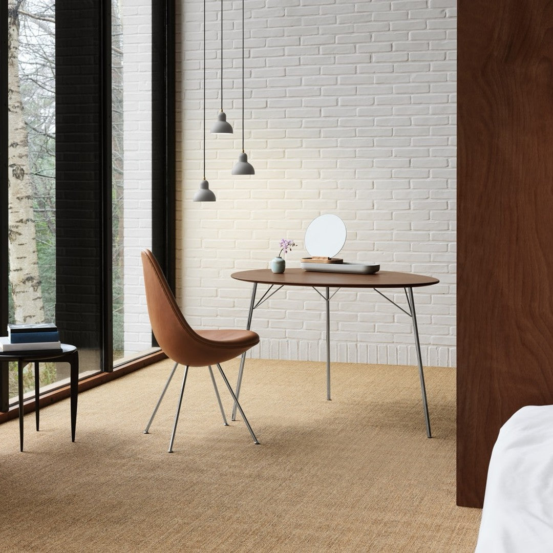 "Cozy brown chair and round wooden table against a textured beige floor and white brick wall, with soft gray pendant lights."