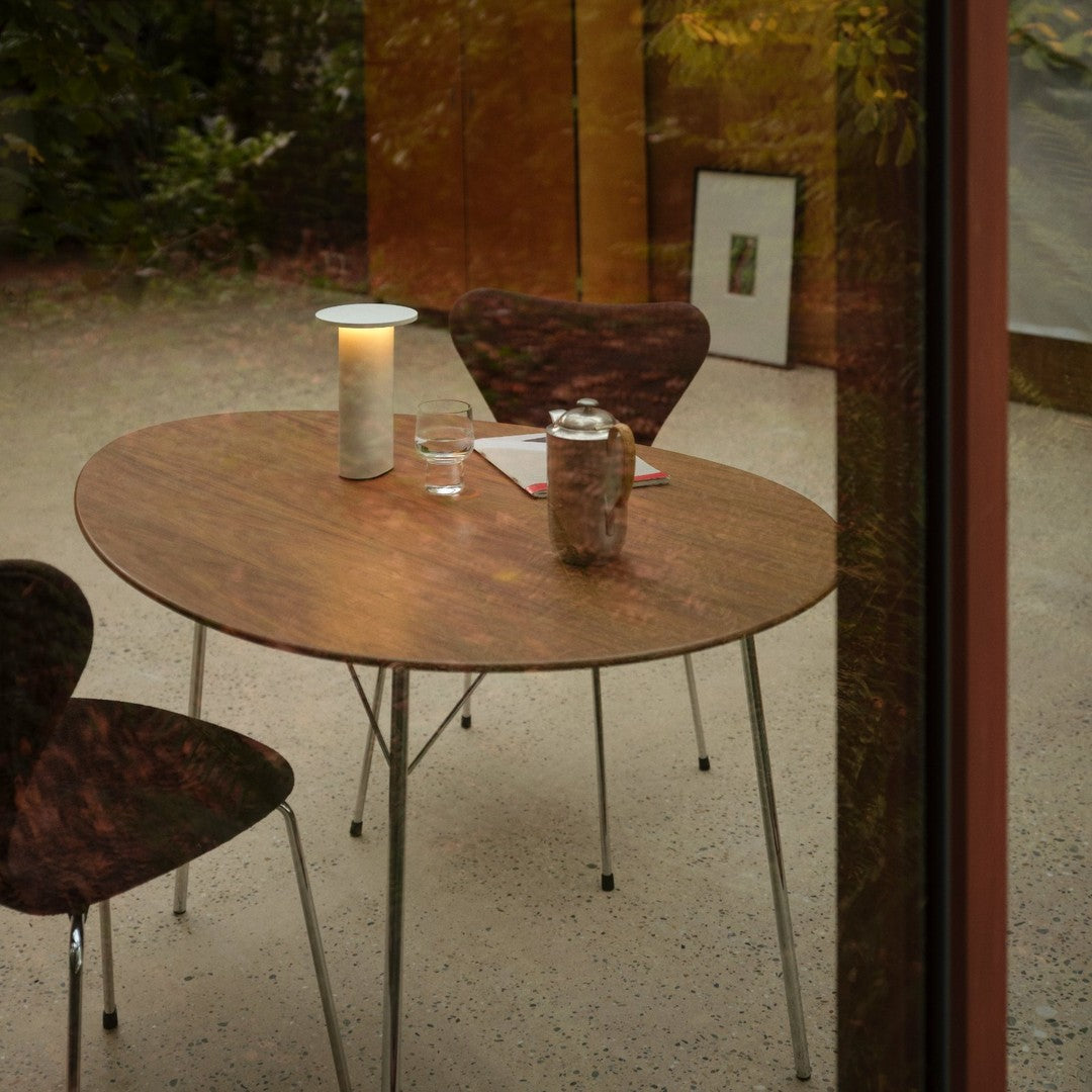 Round wooden table with a smooth finish, complemented by sleek metallic legs and dark patterned chairs.