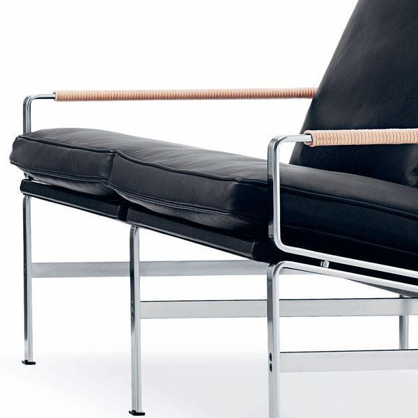 Black leather chaise lounge with chrome accents and natural cane armrests, showcasing a modern, minimalist design.