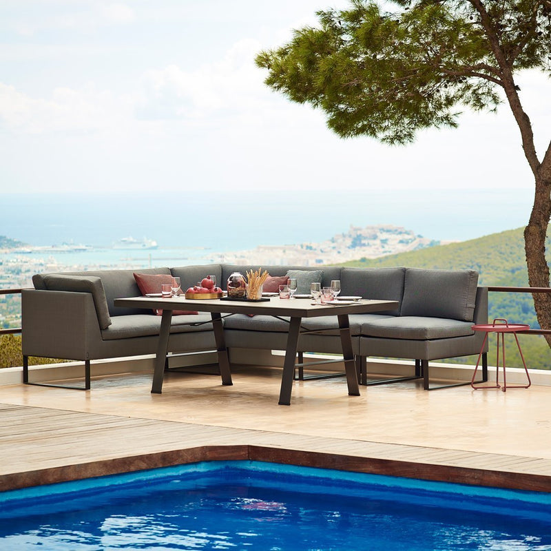 Outdoor gray sectional sofa set with vibrant cushions, black frame, and a scenic backdrop of blue water and greenery.