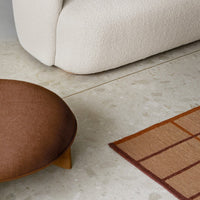Textured beige upholstery, round brown pouf, and a warm-toned checkered rug with earthy tones.