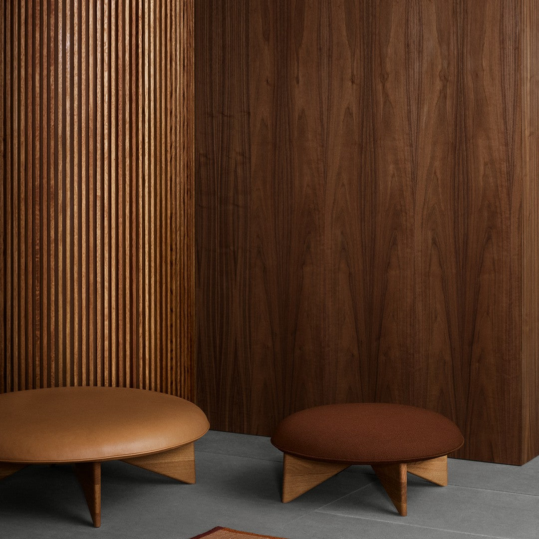 Brown and tan round ottomans against a rich wood panel backdrop, featuring clean lines and modern design elements.