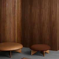 Brown and tan round ottomans against a rich wood panel backdrop, featuring clean lines and modern design elements.