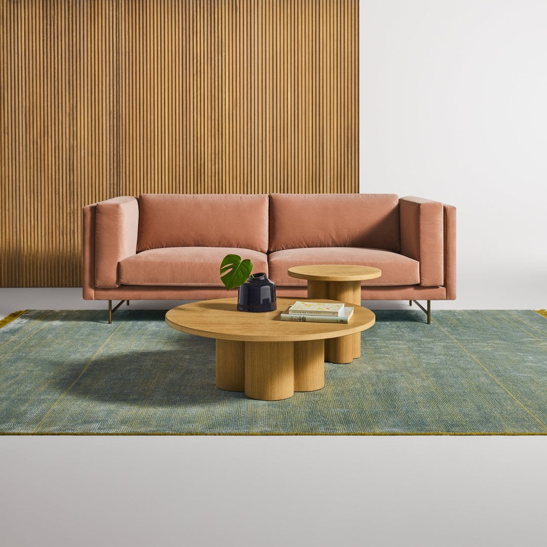 Blush pink sofa on a teal patterned rug with a natural wood coffee table, accented by greenery.