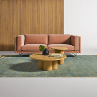 Blush pink sofa on a teal patterned rug with a natural wood coffee table, accented by greenery.