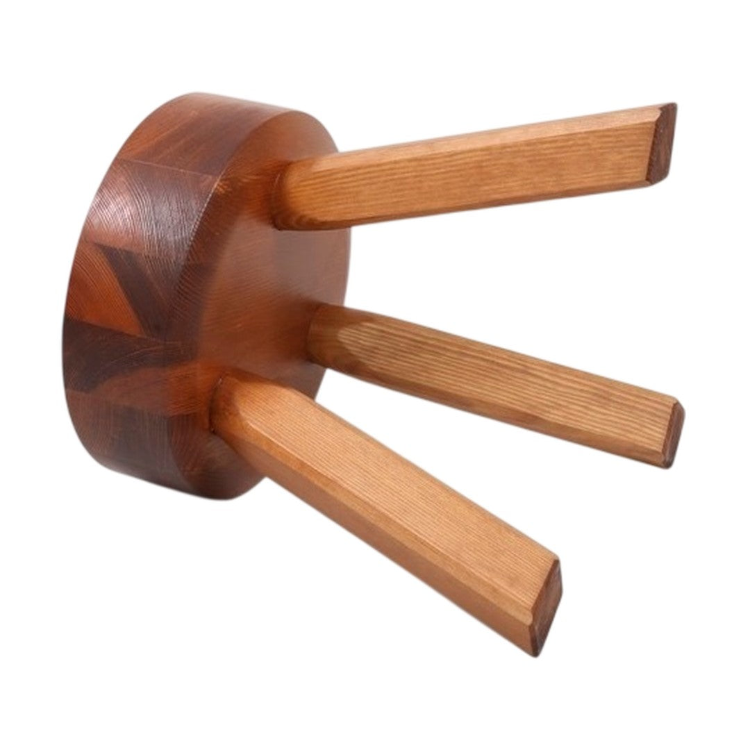 Wooden trivet with dark brown circular base and three light brown tapering legs, showcasing natural wood grain patterns.