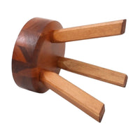Wooden trivet with dark brown circular base and three light brown tapering legs, showcasing natural wood grain patterns.