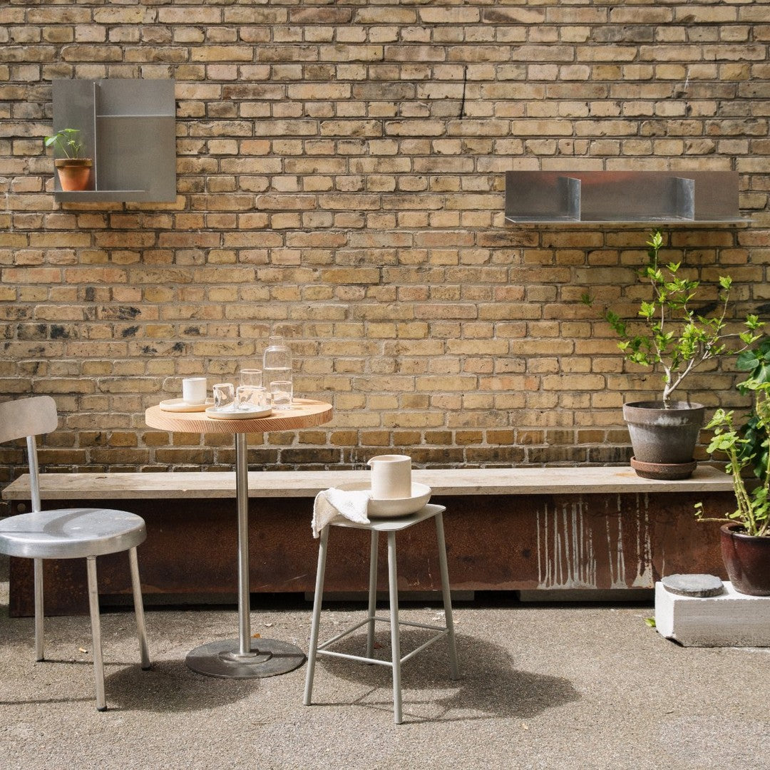 Gray metal furniture with natural wood accents against a textured brick wall, complemented by green plants in pots.