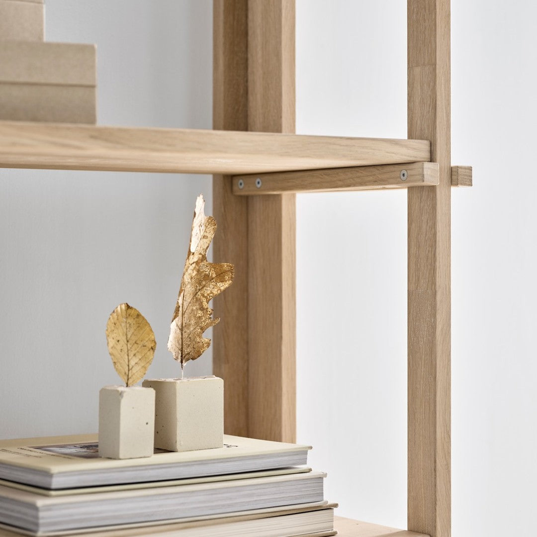 Light wood shelf with neutral-toned blocks and dried leaves against a minimalist white background.