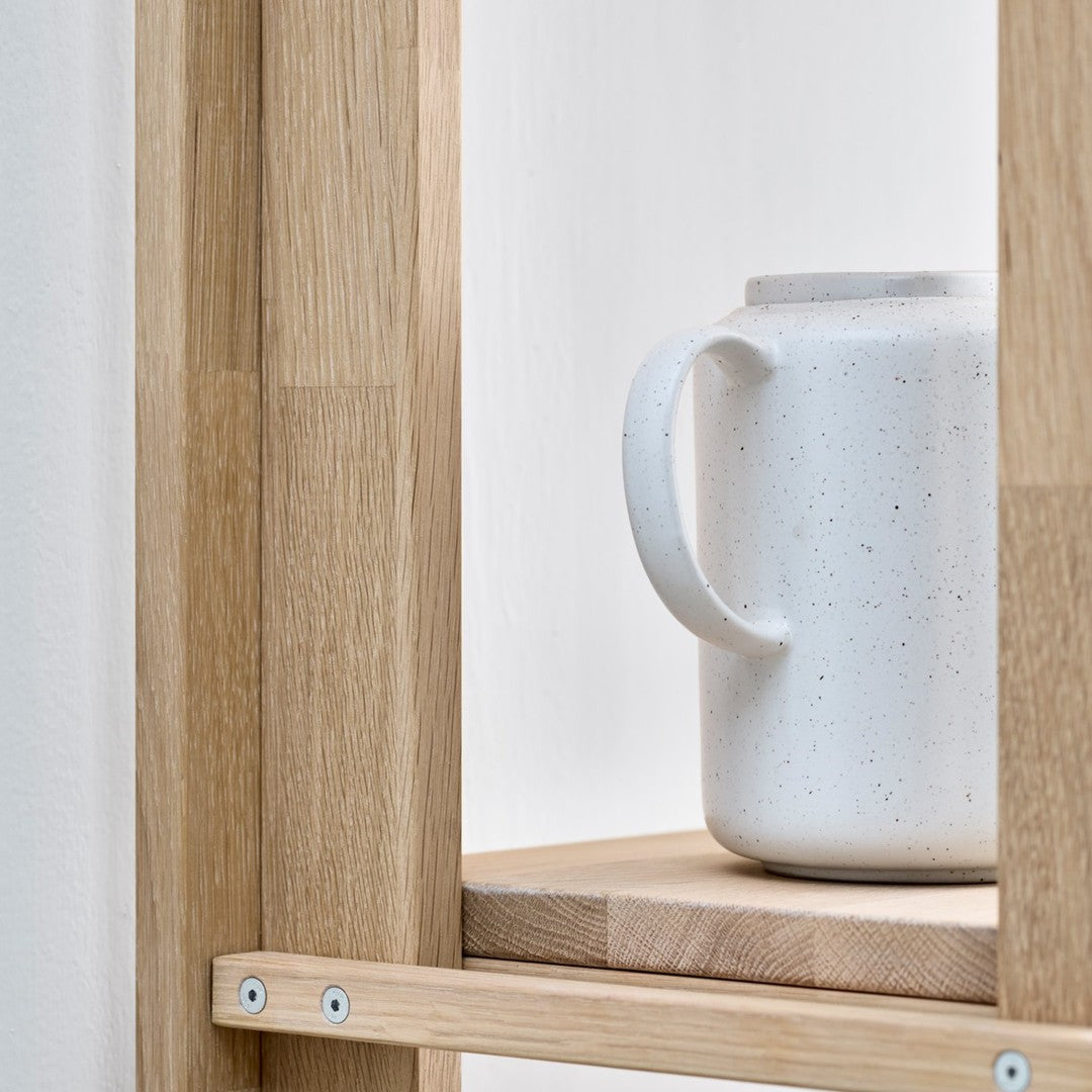White speckled ceramic jug on a natural wood shelf with clean lines and simple aesthetics.