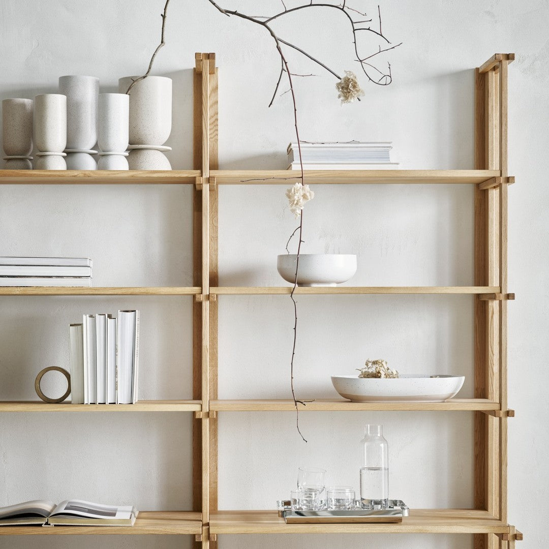 Light wood shelves displaying white ceramics and books with minimalistic design against a neutral wall.
