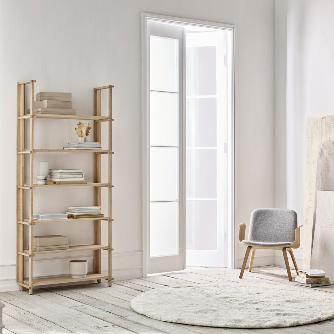 Light wood shelving unit with natural finish, soft gray chair, and cream round rug on light wooden floor.