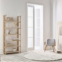 Light wood shelving unit with natural finish, soft gray chair, and cream round rug on light wooden floor.