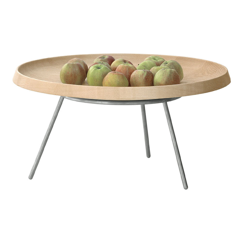 Light wood round serving tray with a smooth finish and silver metal legs, featuring green and red apples on top.