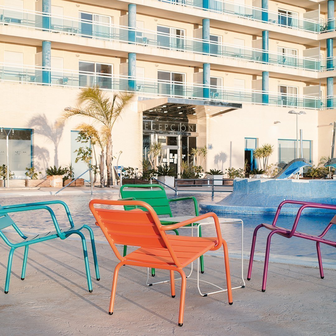 Colorful patio chairs in vibrant teal, orange, green, and purple, arranged around a poolside setting.