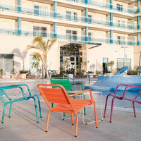 Colorful patio chairs in vibrant teal, orange, green, and purple, arranged around a poolside setting.