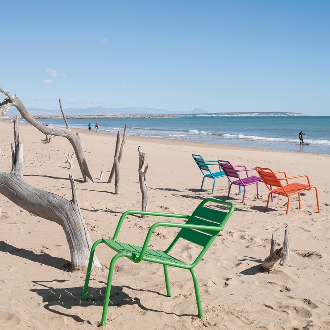 Vibrant beach chairs in green, pink, orange, and purple arranged on sandy shore with ocean backdrop.