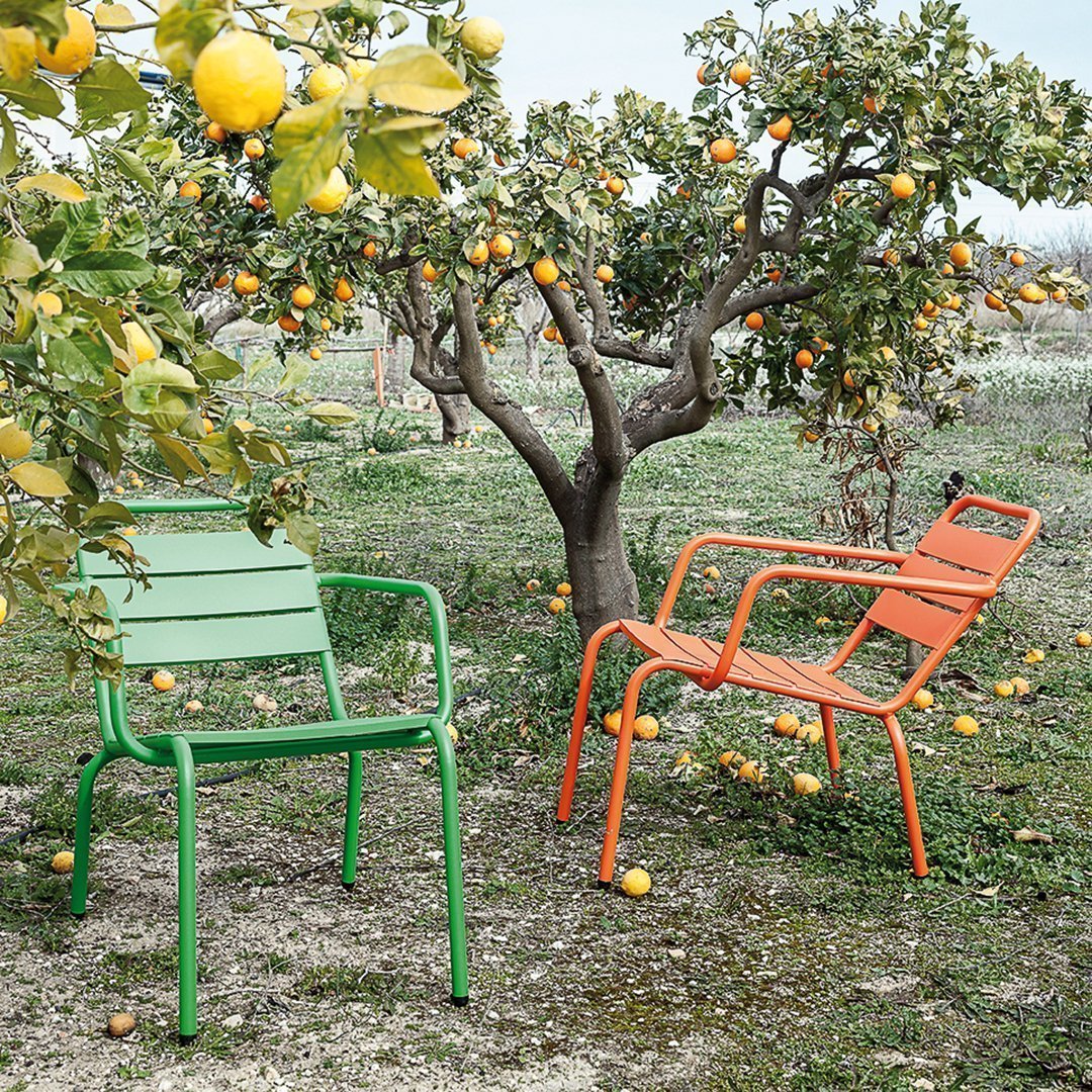 Stylish green and orange metal chairs set against a vibrant orchard backdrop, showcasing a fresh, colorful outdoor aesthetic.