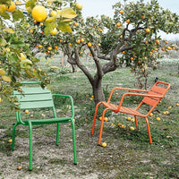 Stylish green and orange metal chairs set against a vibrant orchard backdrop, showcasing a fresh, colorful outdoor aesthetic.