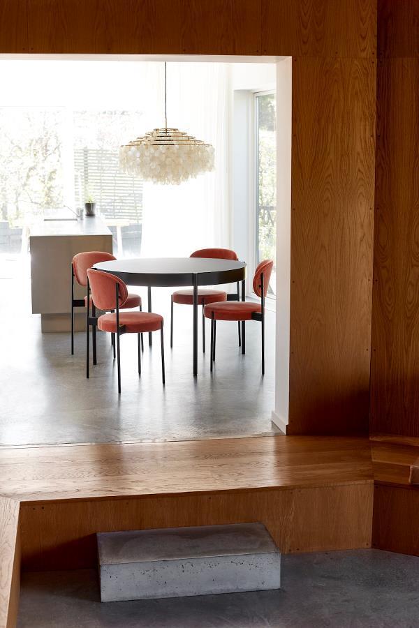 Modern dining room featuring a round black table, orange upholstered chairs, and natural wood accents.