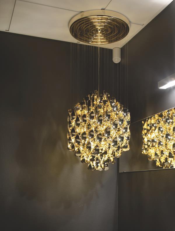 "Elegant gold chandelier with intricate patterns, suspended against a dark wall, creating a stunning contrast."