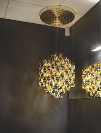 "Elegant gold chandelier with intricate patterns, suspended against a dark wall, creating a stunning contrast."