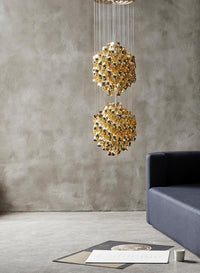 Gold geometric pendant light with intricate patterns, suspended above a modern gray sofa in a minimalist setting.