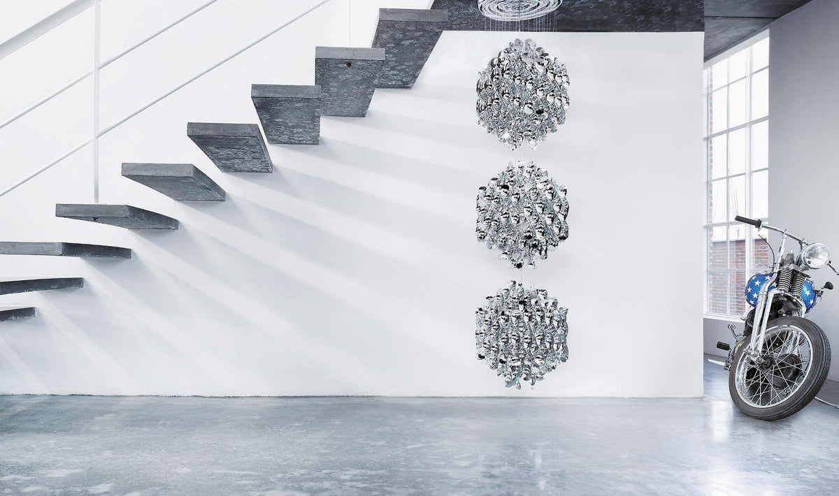 Modern wall art in silver tones with intricate patterns, placed against a white wall and gray stair backdrop.