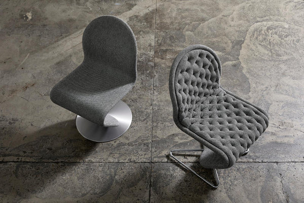 Modern grey upholstered chairs with smooth and tufted textures, set against a rustic concrete backdrop.