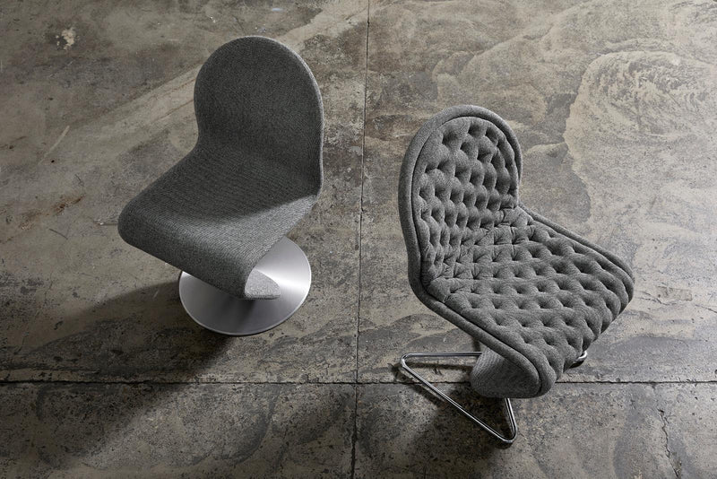 Modern grey upholstered chairs with smooth and tufted textures, set against a rustic concrete backdrop.