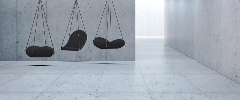 Three sleek, modern black hanging chairs against a minimalist gray concrete wall and floor, showcasing a simple elegance.