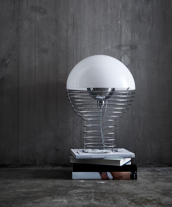 Contemporary lamp with a white dome shade and chrome base, set atop stacked black and white books against a gray backdrop.