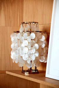 White shell lamp with a layered design, featuring circular patterns and a gold metal base, set against warm wood tones.